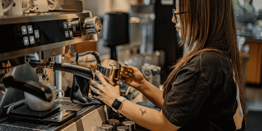 Barista bereitet an einer Siebträgermaschine Kaffee zu und schäumt Milch in einem Café