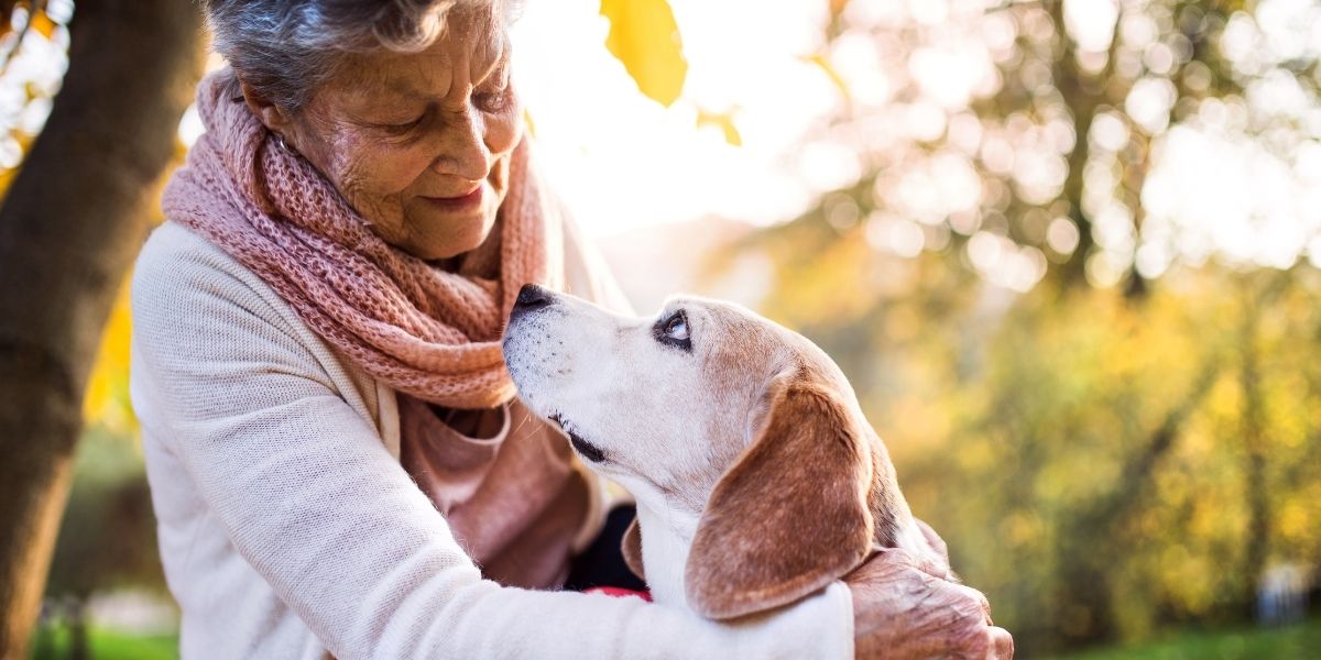 eine ältere Person hält im Freien einen Beagle im Arm; beide blicken sich an.