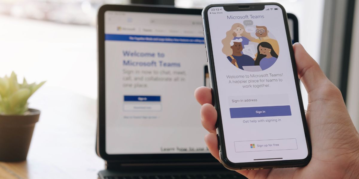 Eine Hand, die, vor einem Laptop, ein Smartphone mit Microsoft Teams hält