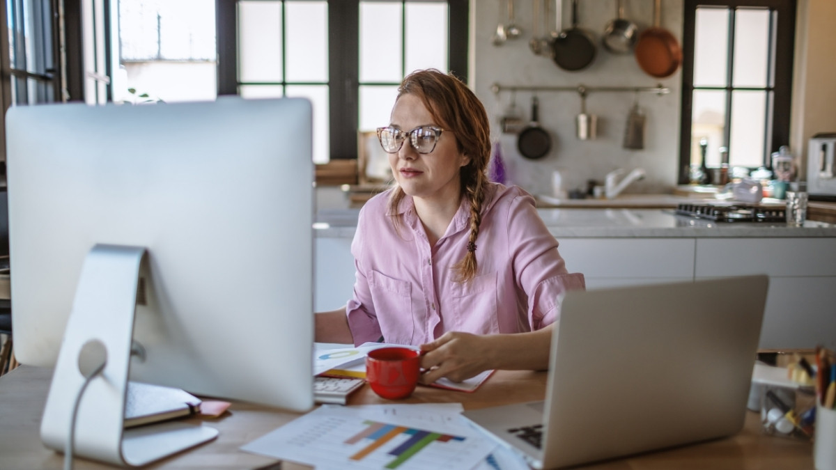 Frau arbeitet im Homeoffice an Computer und Laptop in einer Küche