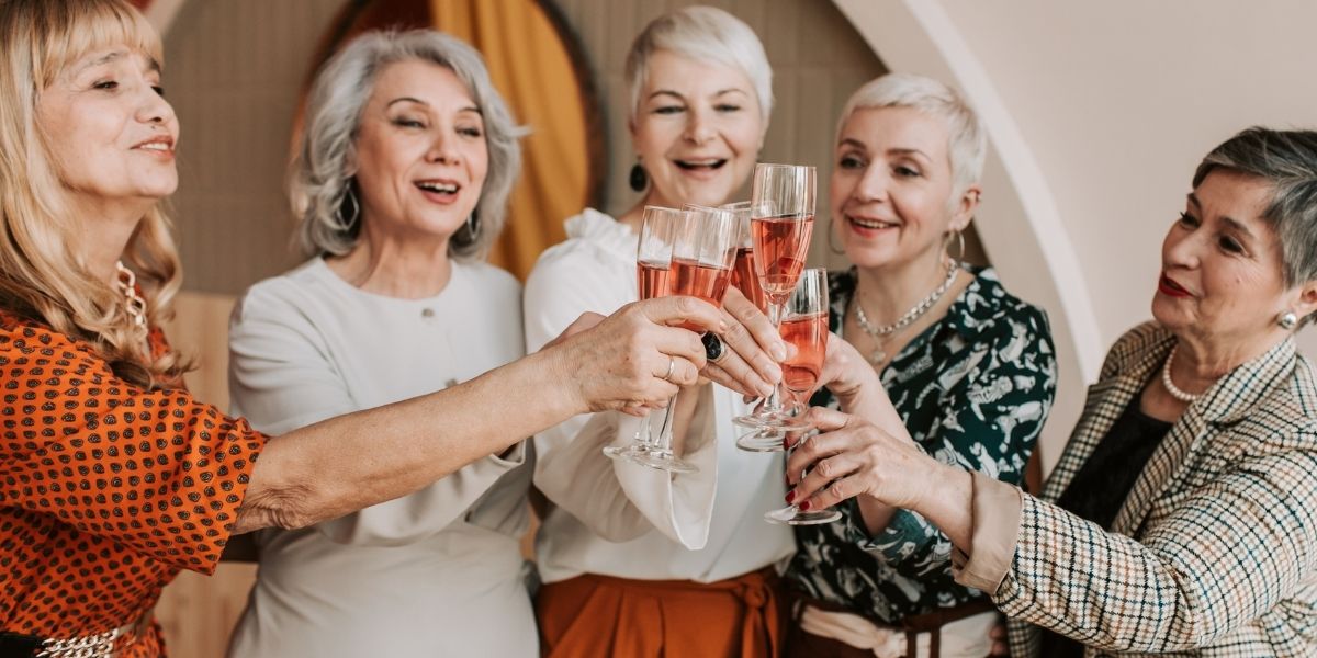 Fünf Frauen über 60 Jahren stoßen mit einem orangfarbenen Getränk an.