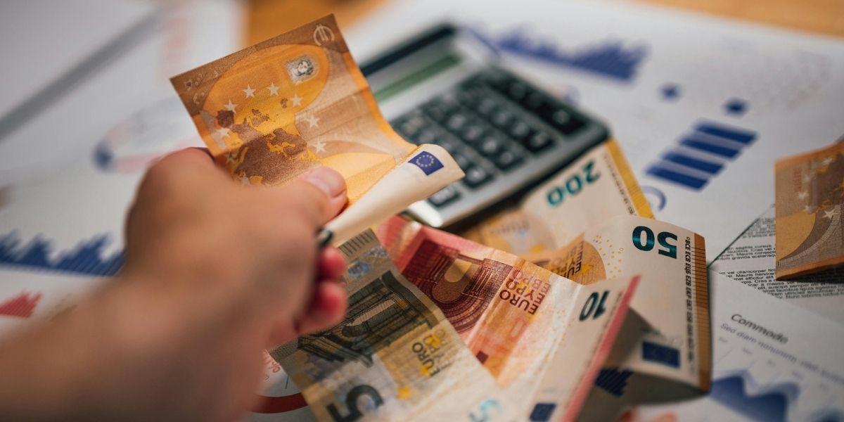 Hand zählt Euro-Banknoten vor Taschenrechner und Finanzunterlagen.
