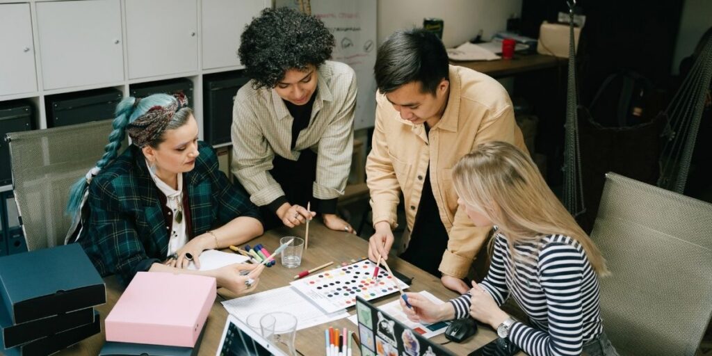 Vier Personen besprechen Farbmuster und Notizen an einem Besprechungstisch in einem Büro.
