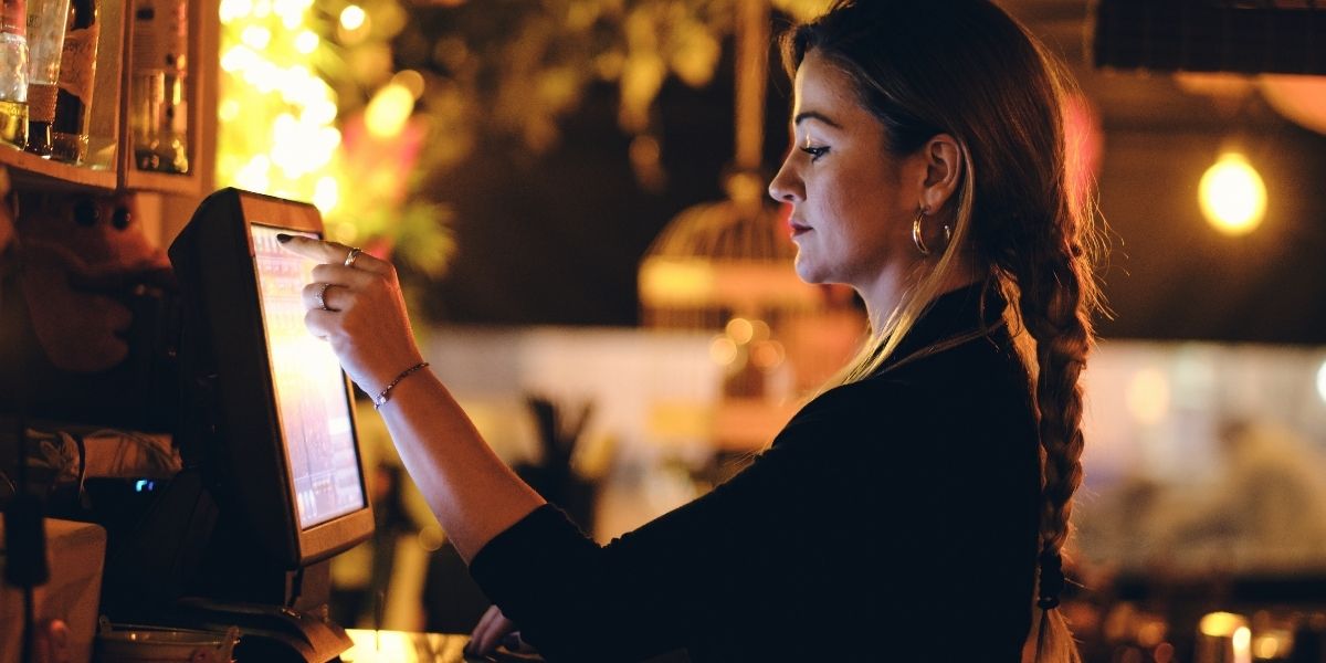 Person bedient Kassensystem mit Touchscreen in warm beleuchteter Gastronomieumgebung.