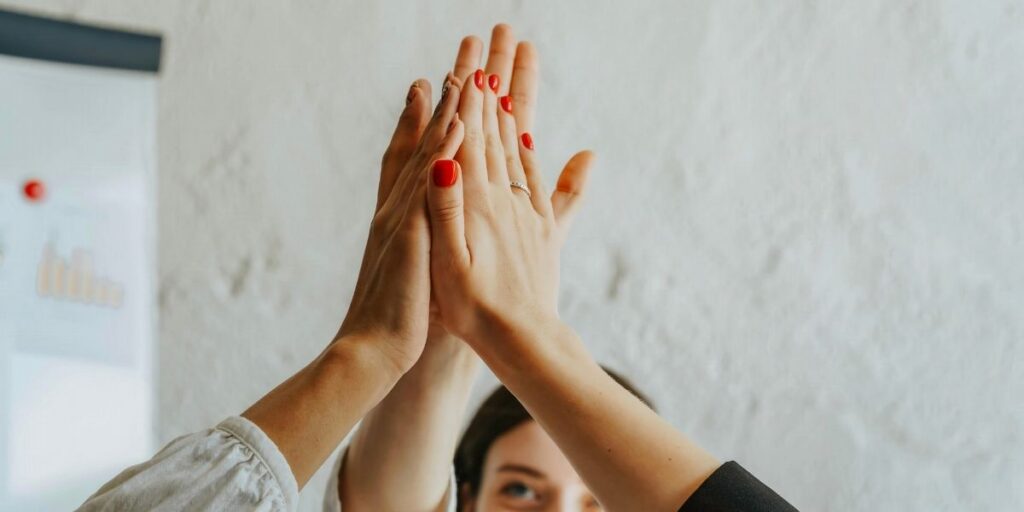 Mehrere Hände berühren sich zu einem High-Five vor heller Innenwand.