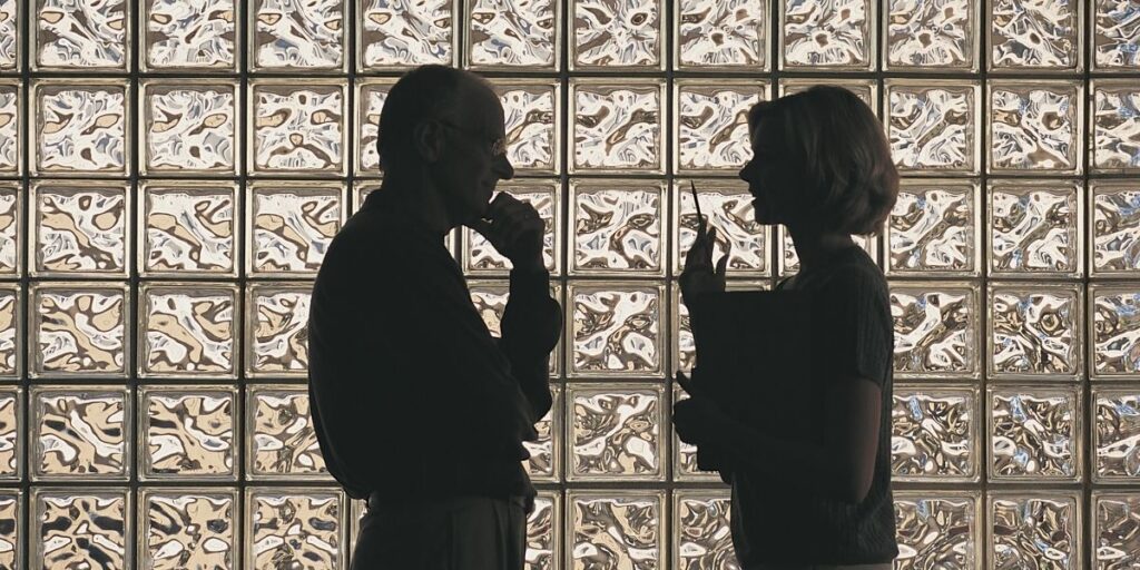 Silhouetten von zwei Personen im Gespräch vor einer Wand aus Glasbausteinen.