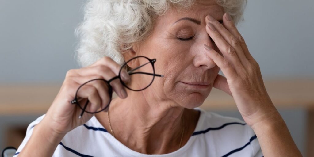 Ältere Frau hält Brille und berührt ihre Stirn