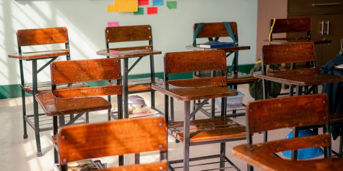 Leeres Klassenzimmer mit mehreren Holz-Schulbänken, Sonnenlicht auf dem Boden und Haftnotizen an der Wand.