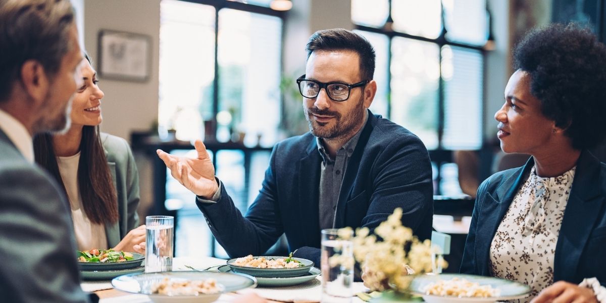 Eine Gruppe von Geschäftsleuten teilt sich eine Mahlzeit in einem Restaurant und unterhält sich freundlich an einem Tisch.