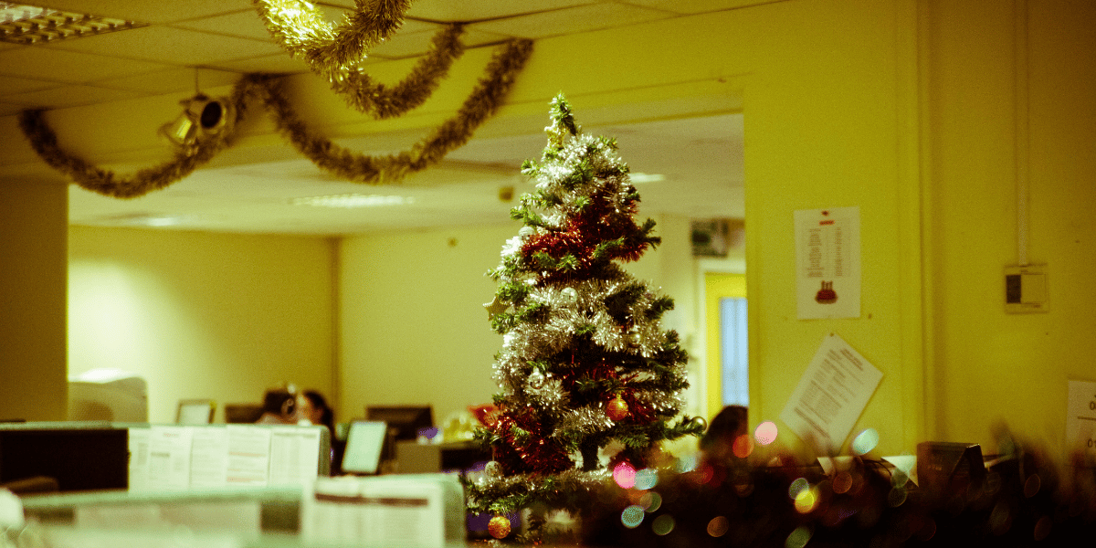 Weihnachtsbaum mit silber- und rotfarbener Dekoration in einem Büro, im Hintergrund Arbeitsplätze und festliche Girlanden an der Decke.