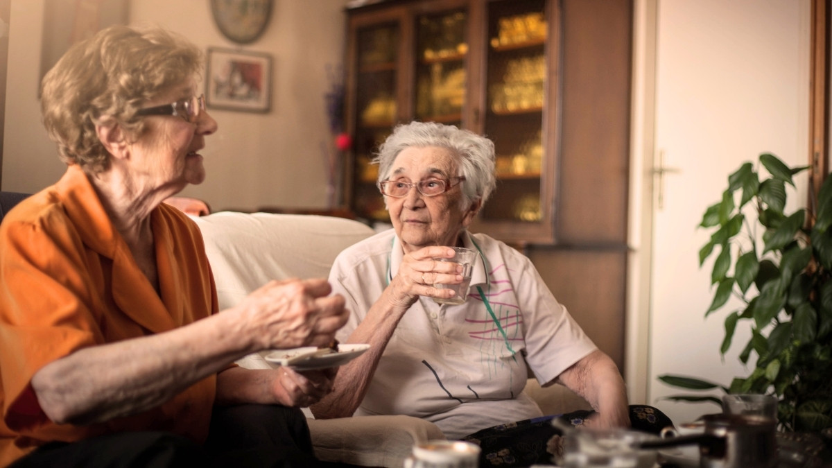 Zwei ältere Frauen sitzen im Wohnzimmer und trinken gemeinsam Kaffee.