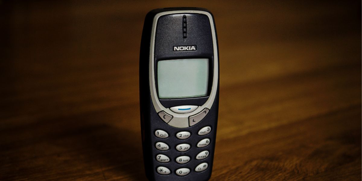 Nokia 3310 Mobiltelefon mit Tastenfeld und monochromem Display, aufrecht auf einer Holzoberfläche stehend.