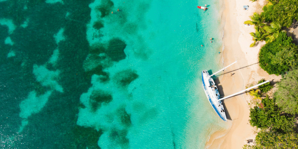 Luftaufnahme eines wei&szlig;en Sandstrands mit t&uuml;rkisfarbenem Meer und einem Segelboot am Ufer einer tropischen Insel.
