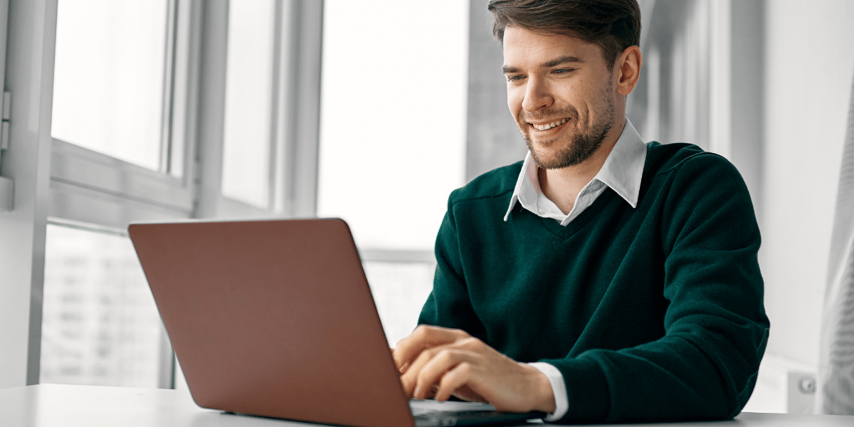 Person tippt lächelnd in einen Laptop in einem hellen Raum.