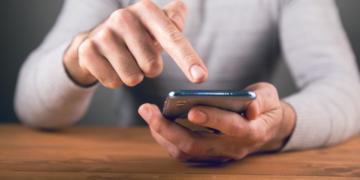 Person bedient mit dem Finger ein Smartphone, das sie in der Hand hält.