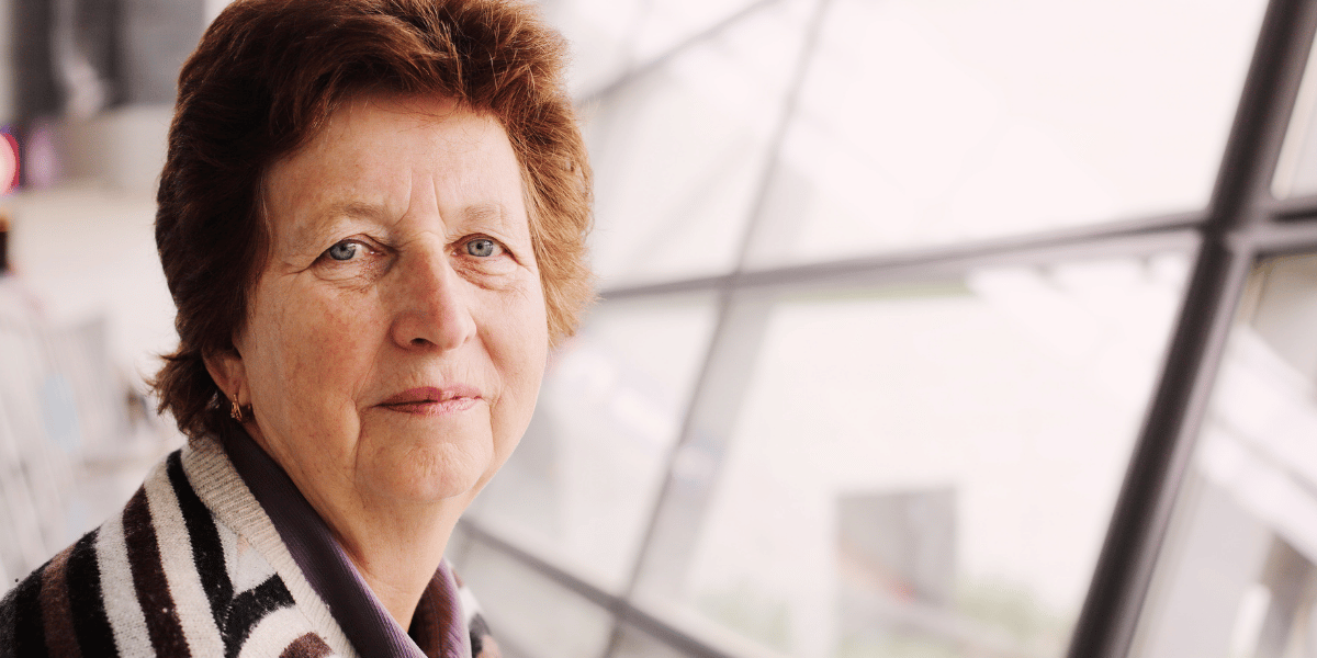 Portrait einer 70 Jahre alten Frau vor einer Glasfassade.