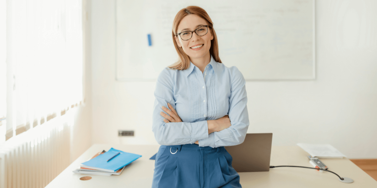 Eine Lehrerin lehnt mit verschr&auml;nkten Armen am Pult.