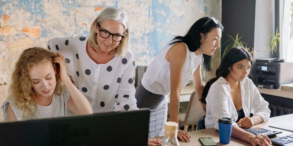 Vier Kolleginnen unterschiedlichen Alters arbeiten gemeinsam an einem Computer in einem hellen B&uuml;ro.