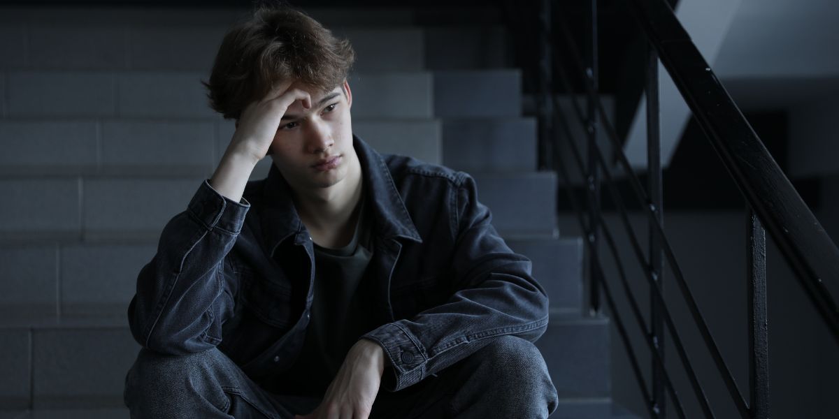 Ein junger Mann sitzt nachdenklich auf einer Treppe und stützt den Kopf auf eine Hand.