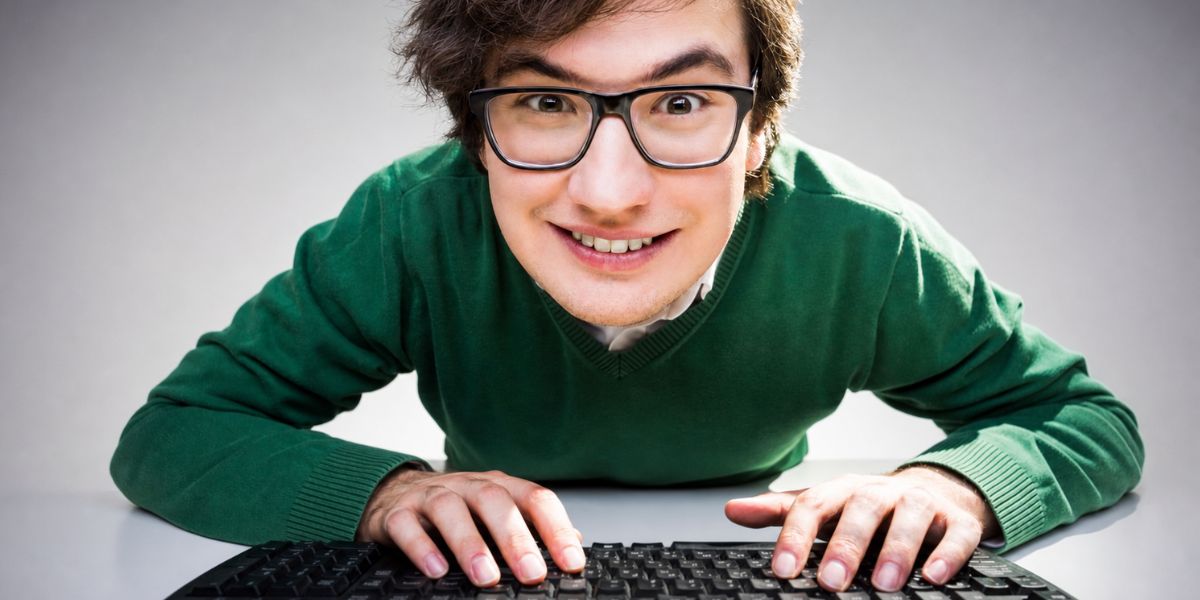 Junge Person mit Brille grinst und starrt, während die Hände auf einer schwarzen Tastatur liegen