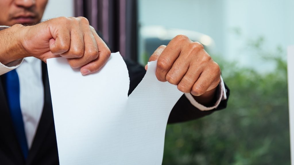 Ein Mann im Anzug zerei&szlig;t ein St&uuml;ck Papier mit seinen H&auml;nden
