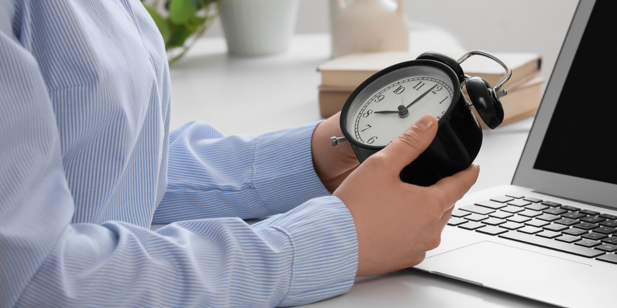 Mann im hellblauen Hemd hält eine analoge Uhr in seiner Hand